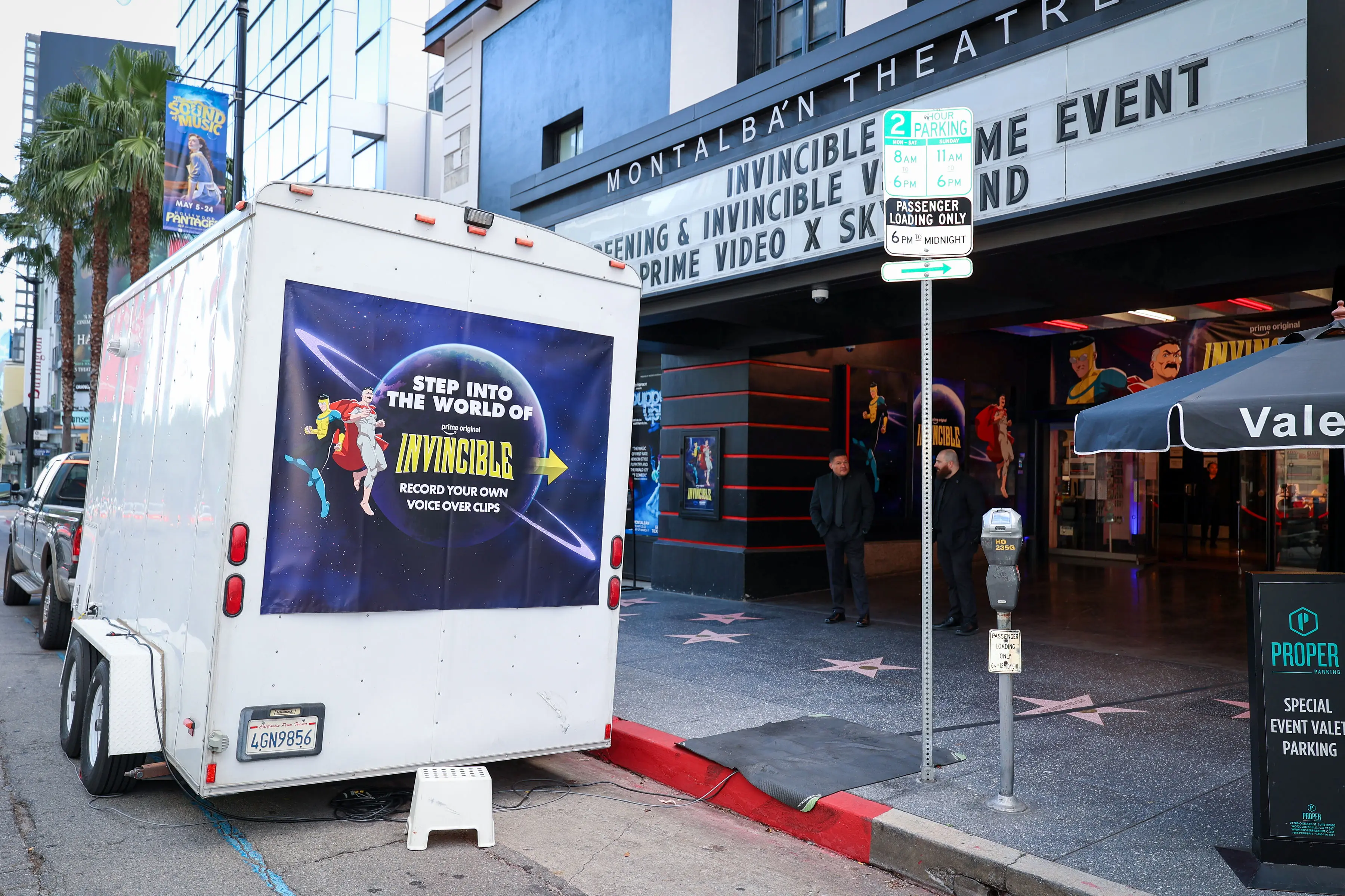 White branded trailer parked outside the Montalbán Theatre with a large 'Step into the World of Invincible' vinyl decal inviting passersby to record voice-over clips during an Invincible screening event.