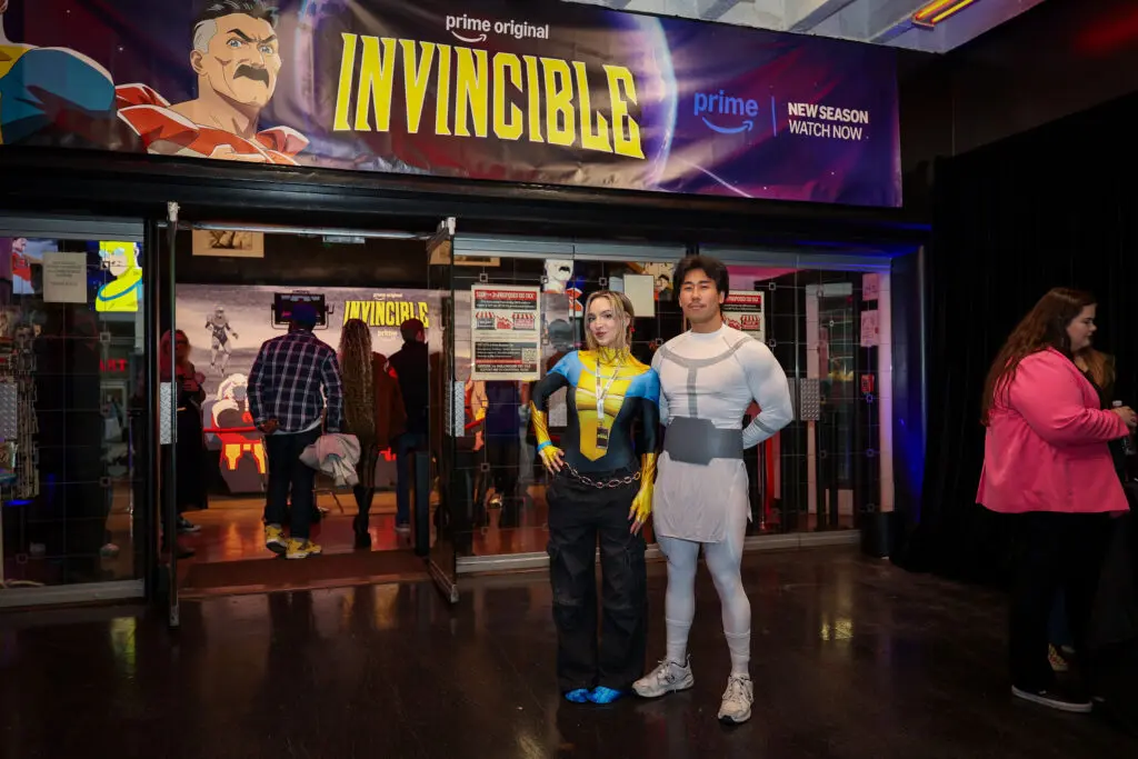 Creators @justinsaiyann and @missbrisolo pose in costume beneath Invincible event signage at the entrance to the creator screening experience.