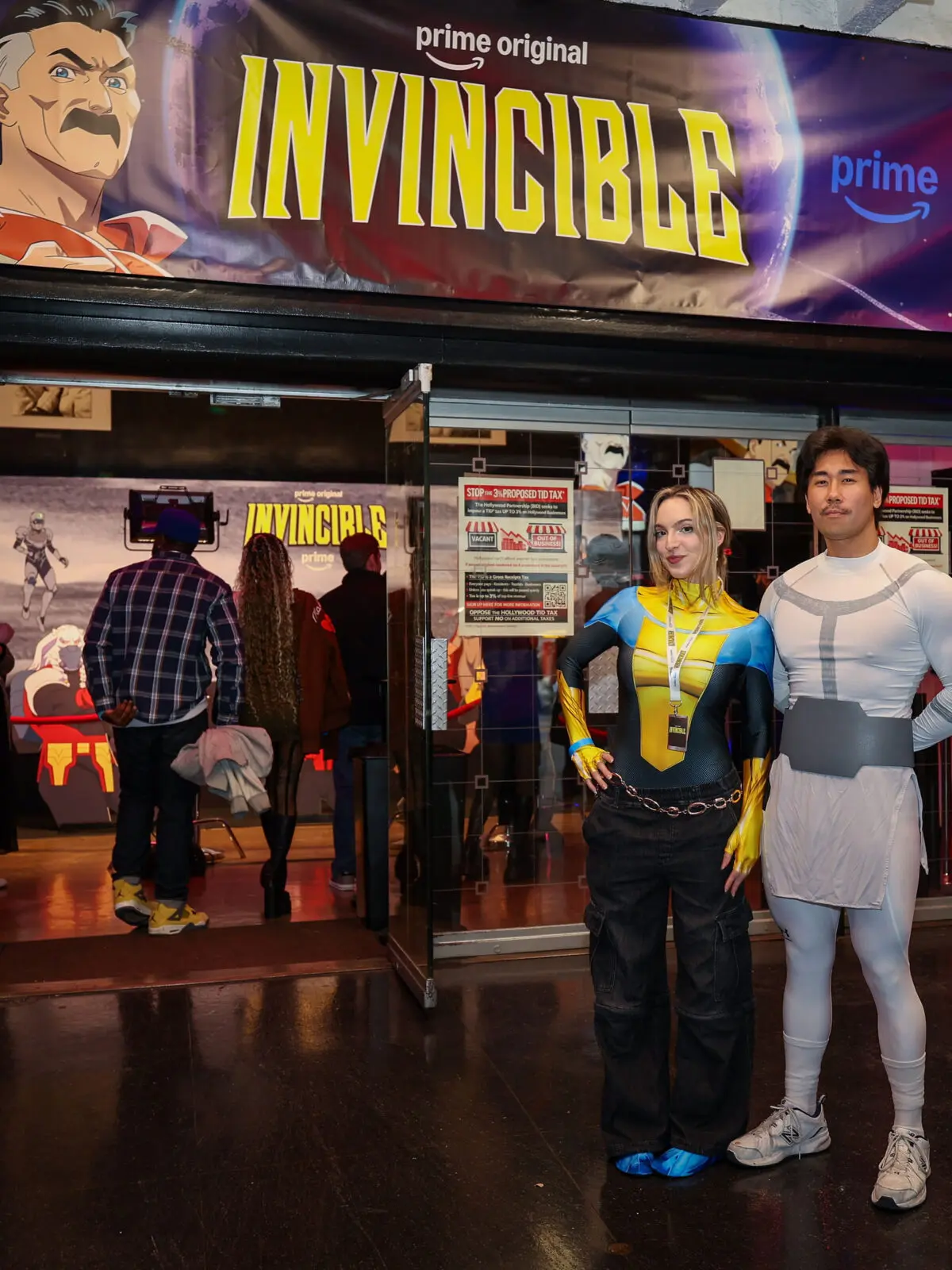 Creators Miss Brisolo and Justin Saiyann pose in costume beneath a large Invincible Prime Video marquee at the branded Season 4 screening event.