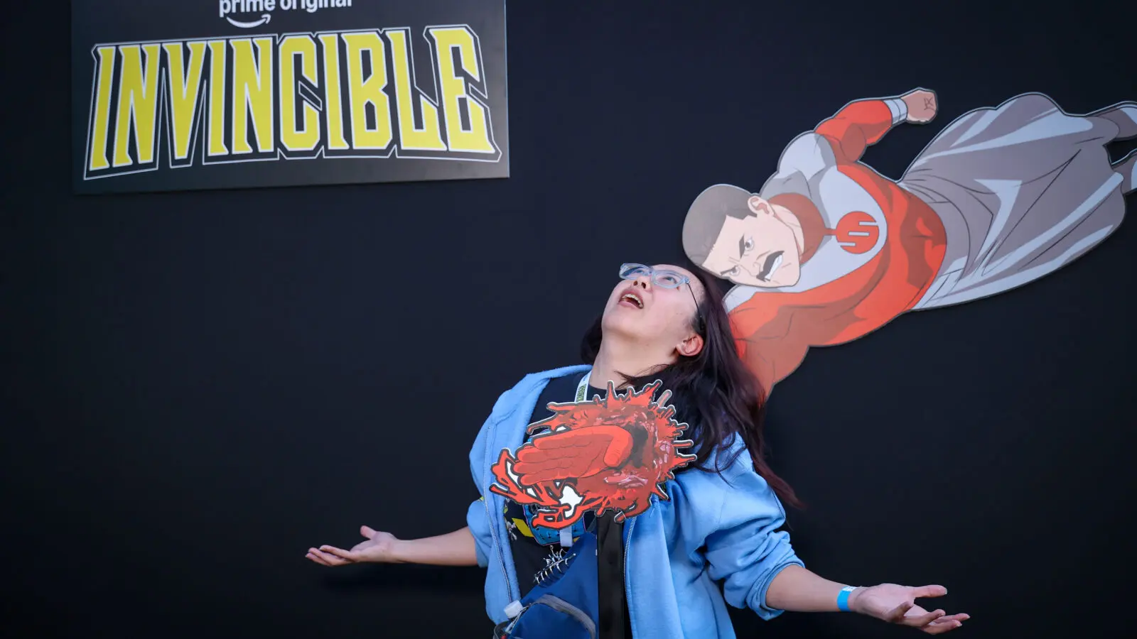 A guest poses as though Thragg has punched through their chest in an interactive Invincible photo installation featuring an in-house illustrated character cutout and dimensional impact prop.