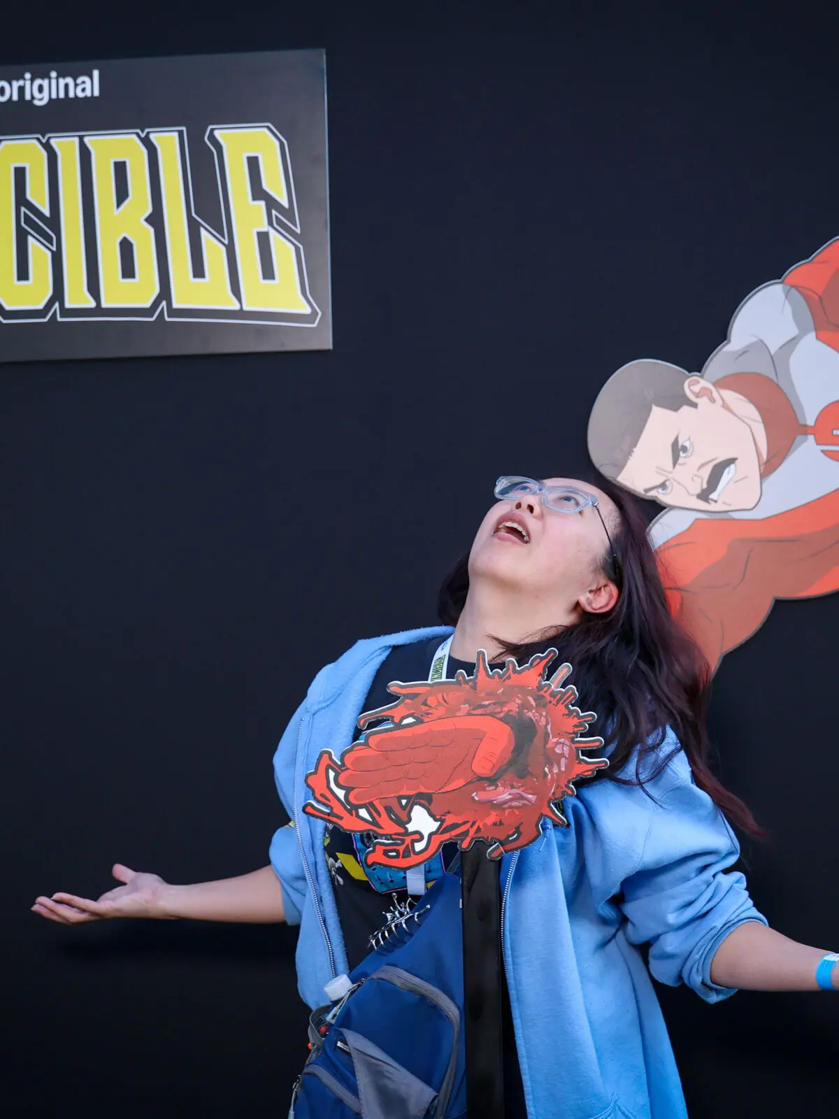 A guest poses as though Thragg has punched through their chest in an interactive Invincible photo installation featuring an in-house illustrated character cutout and dimensional impact prop.