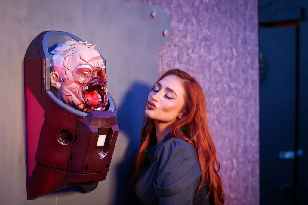 Rebecca Seals poses beside a life-size, battle-damaged Conquest head installation mounted in a GDA-style display at the Invincible creator screening.