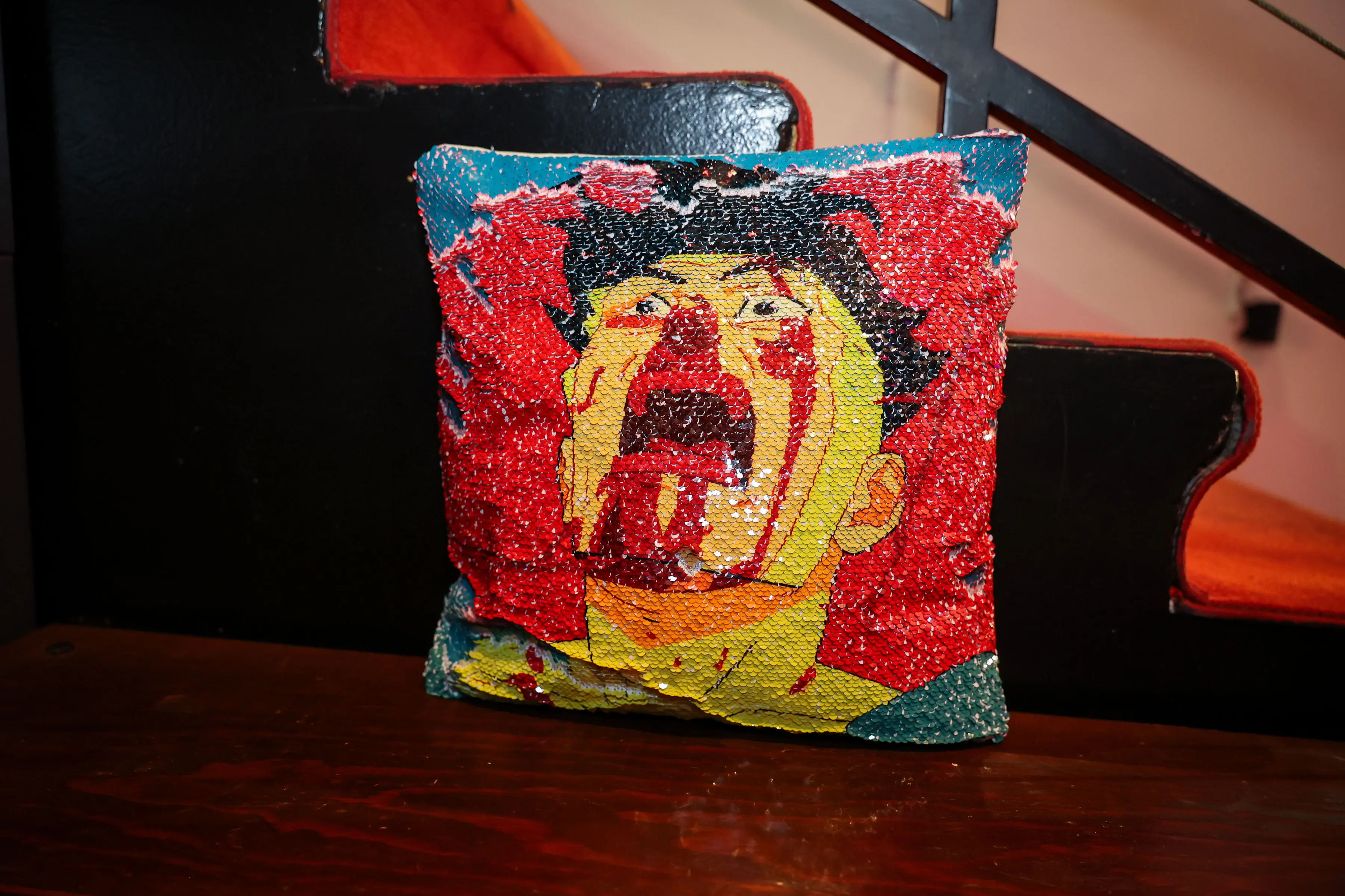 A red throw pillow features a blood-splattered illustration of a screaming yellow-suited character, displayed on a black chair in the Invincible creator screening lounge.