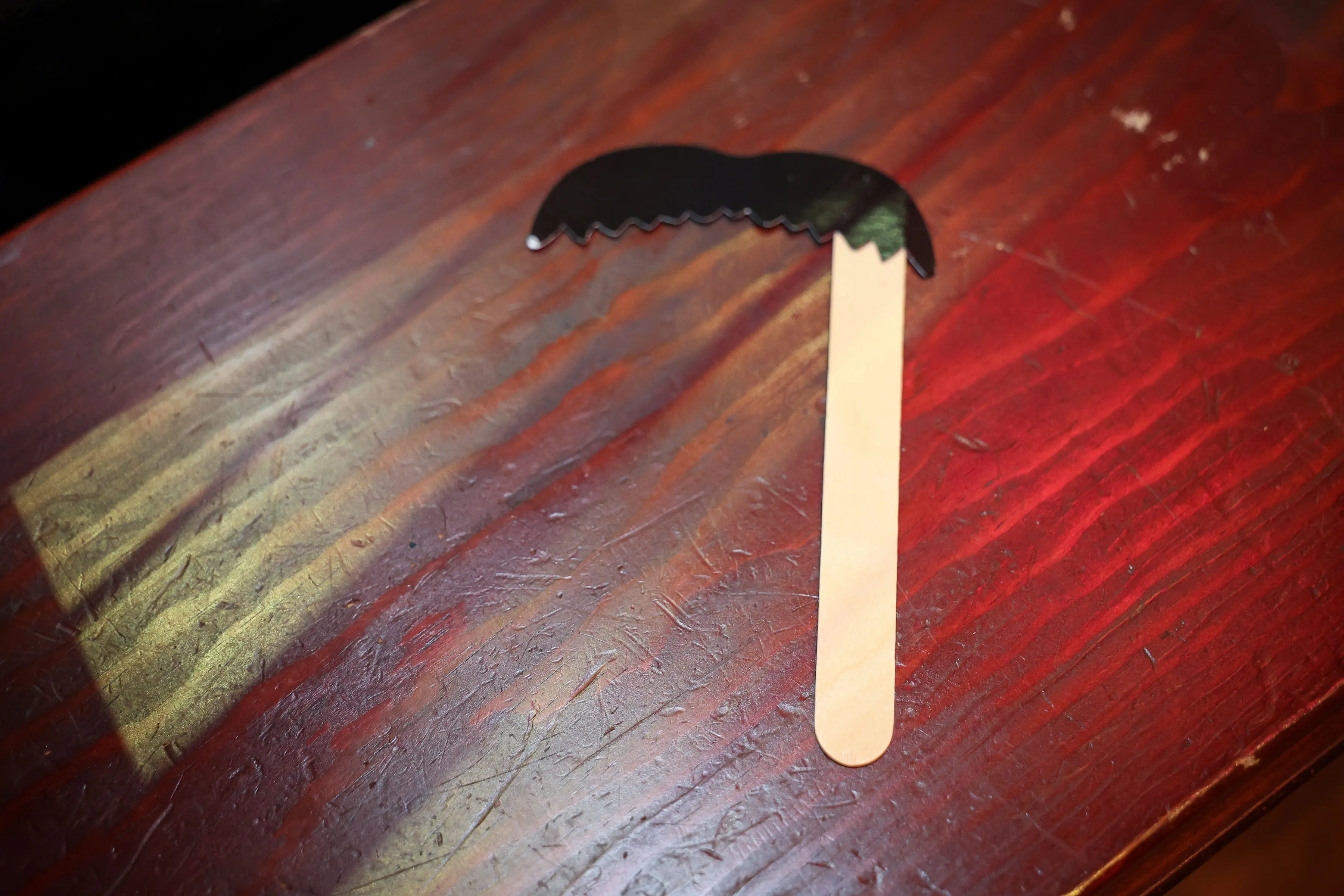 A black mustache-shaped prop on a wooden stick rests on a scratched, red-lit tabletop at the Invincible creator screening experience.