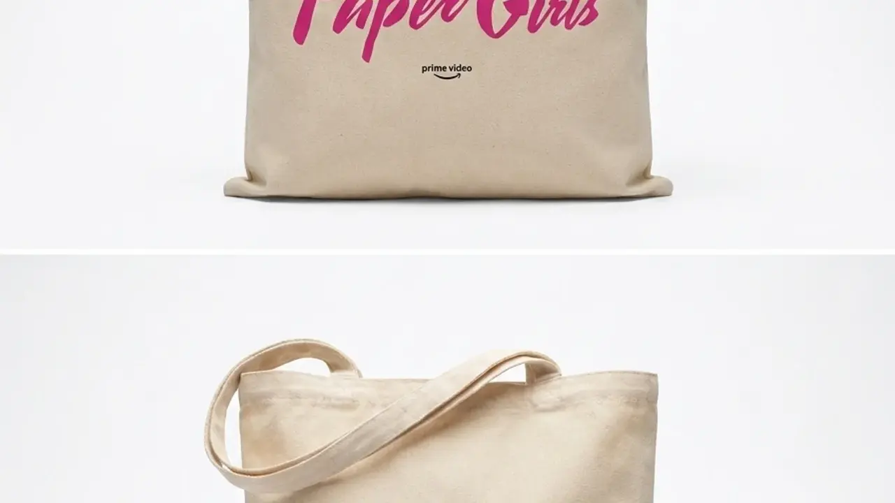 Natural canvas tote shown front and back: top face has a hot-pink hand-lettered 'Paper Girls' logo with Amazon Original and Prime Video mark; reverse shows black Gothic 'The Cleveland Preserver' masthead.