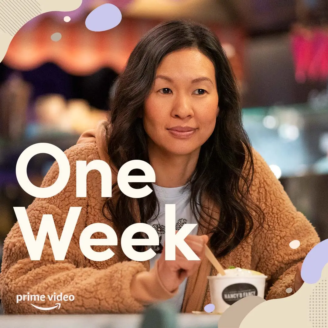 Violet sits at a cafe table wearing a tan sherpa jacket, stirring a cup of ice cream while large white text reading "One Week" overlays a warm, softly blurred background.