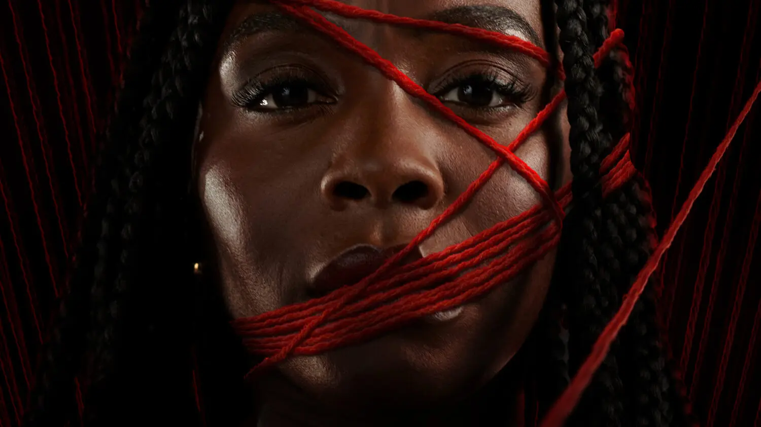 Close-up portrait of Deborah Ayorinde surrounded by strands of red yarn for Prime Video’s THEM: The Scare, set against a dark, textured background.