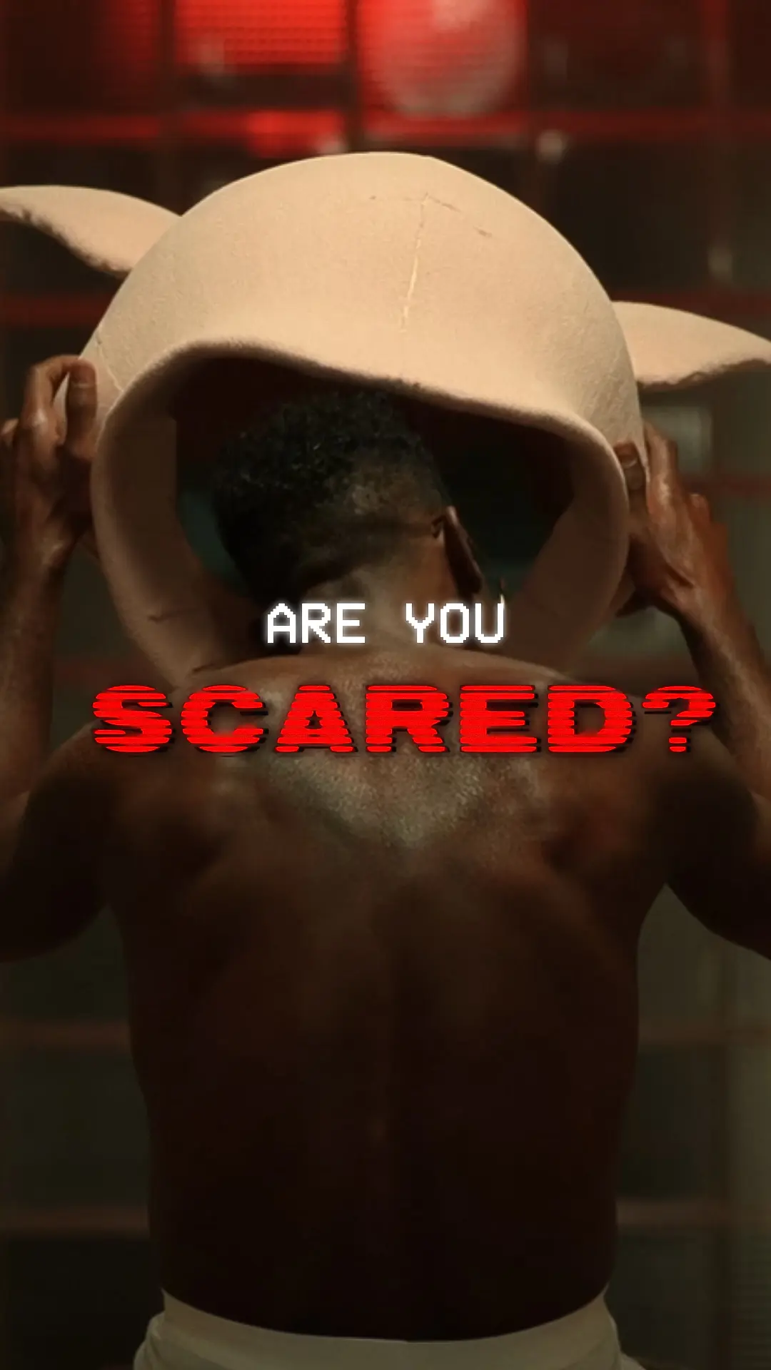Shirtless Black man seen from behind lifting a large pale pig-shaped mask over his head with glitchy red and white text reading 'ARE YOU SCARED?' across the center.