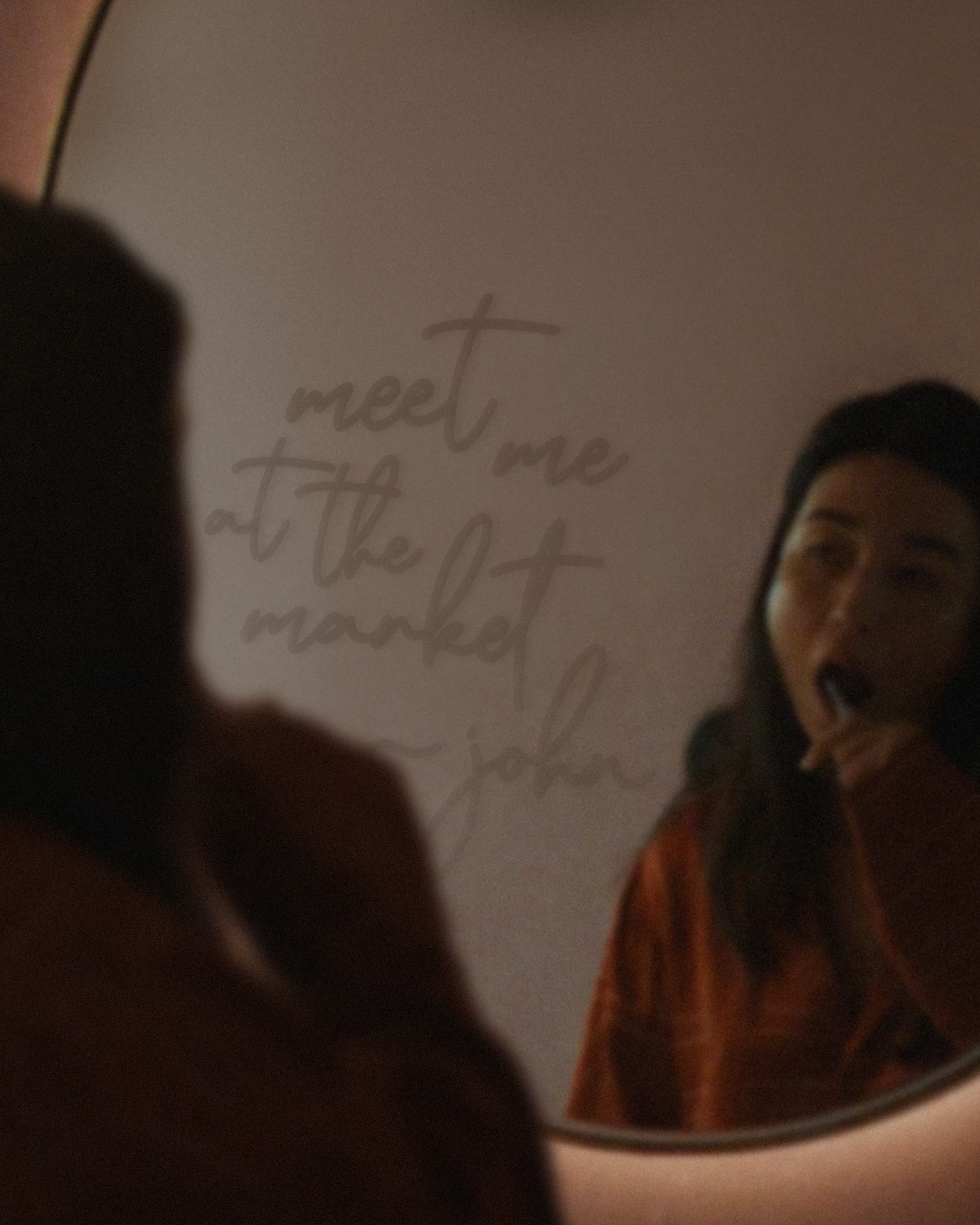 Woman brushing her teeth reflected in a round mirror, with handwritten script saying "meet me at the market - john" faintly visible on the mirror surface in warm, dim light.