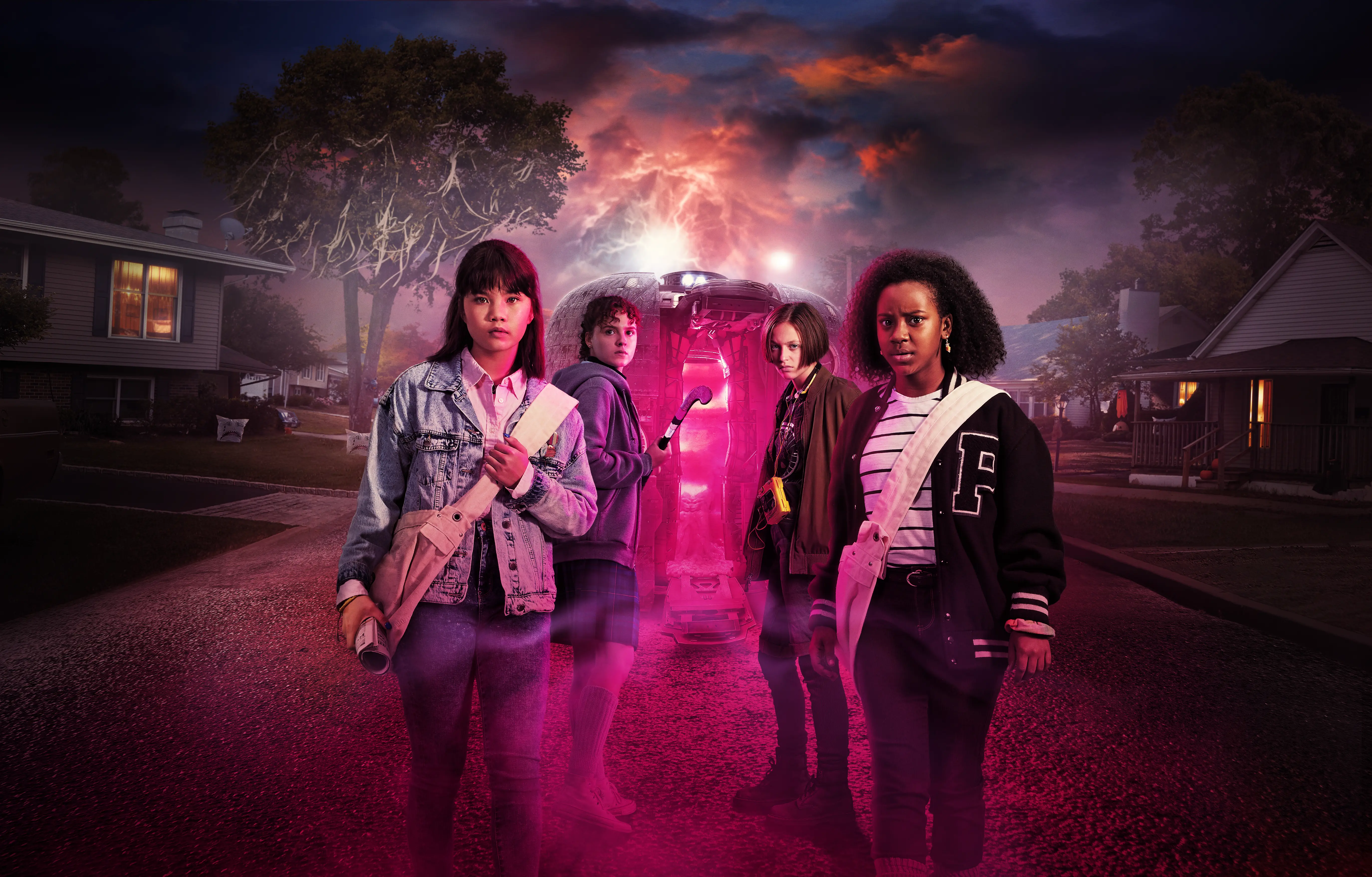 Four teenage girls stand across a suburban street at dusk, carrying newspaper satchels while a glowing pink time-travel pod opens behind them under a stormy, neon-lit sky.