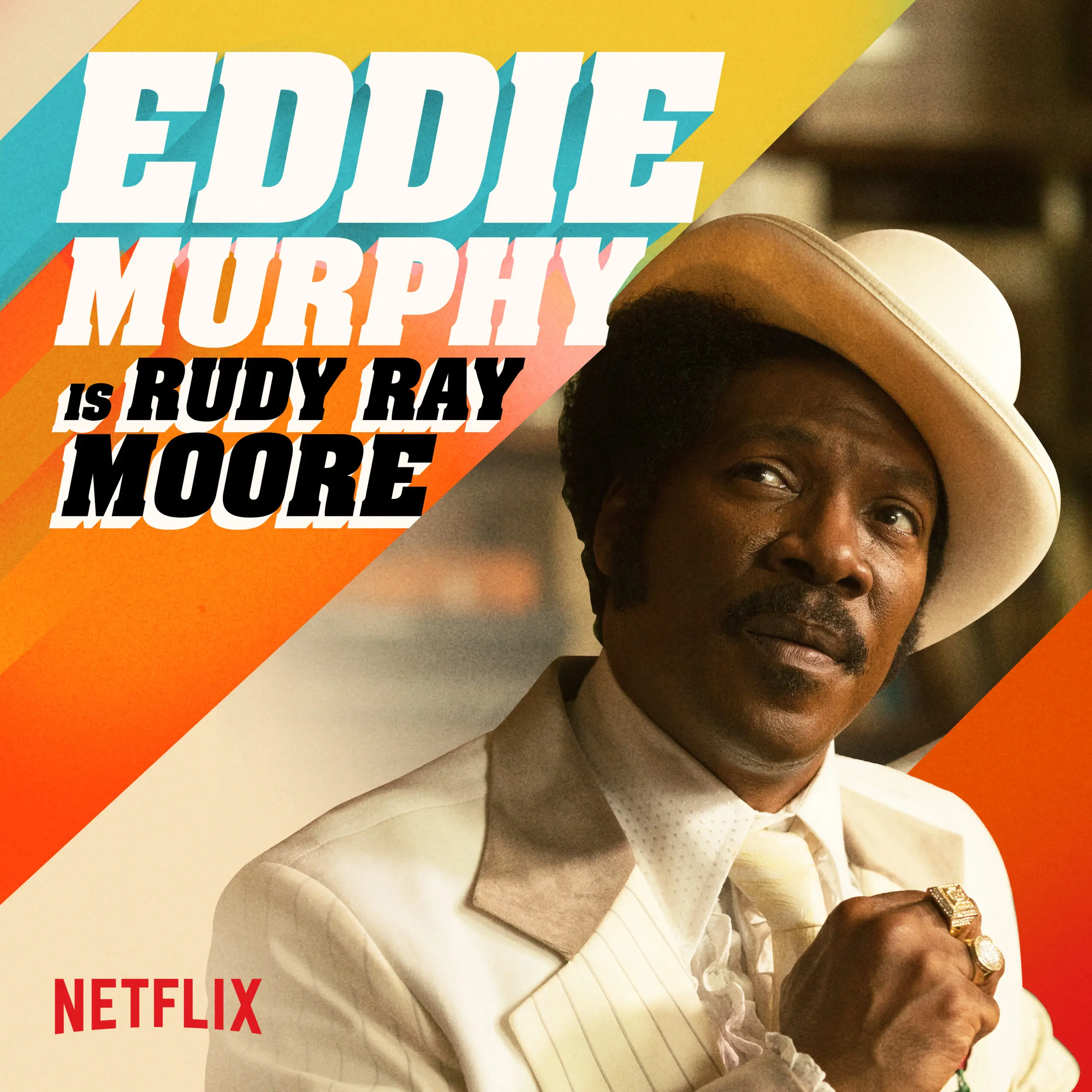 Eddie Murphy in a cream suit and white hat looking to the right, set against diagonal saturated 1970s-style orange and teal stripes with bold 'EDDIE MURPHY is RUDY RAY MOORE' title and Netflix logo.