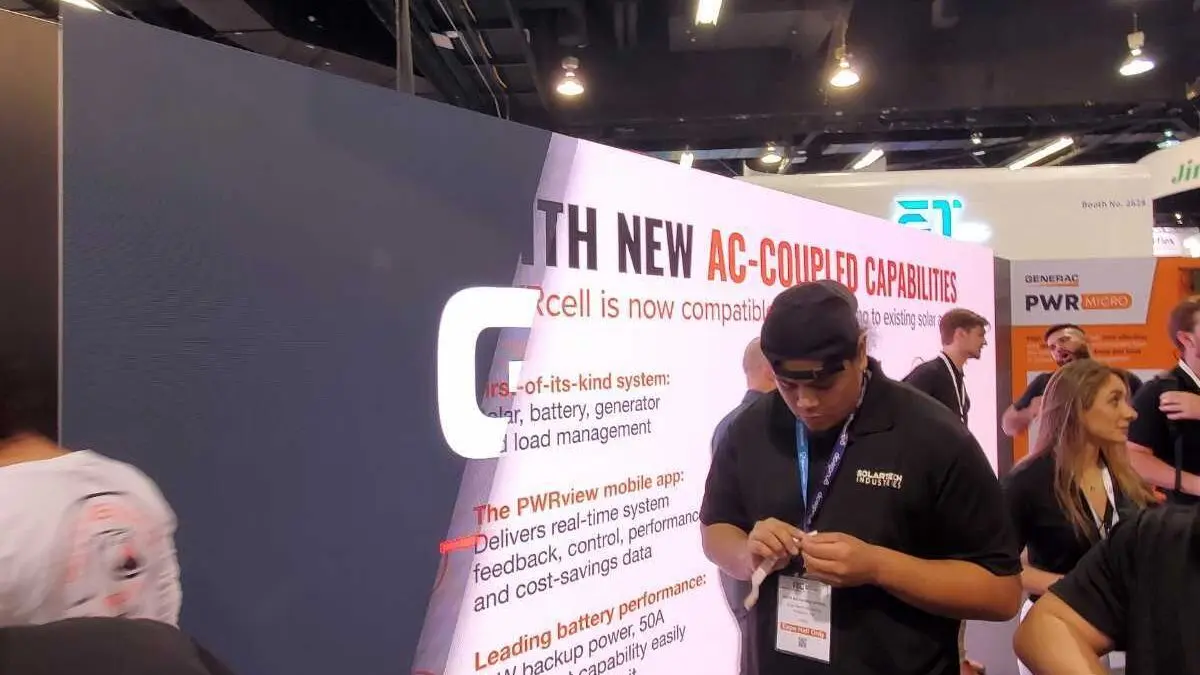 Curved LED video wall at a Generac trade-show booth displaying large copy about AC-coupled PWRcell capabilities, with attendees standing nearby and reading the on-screen information.