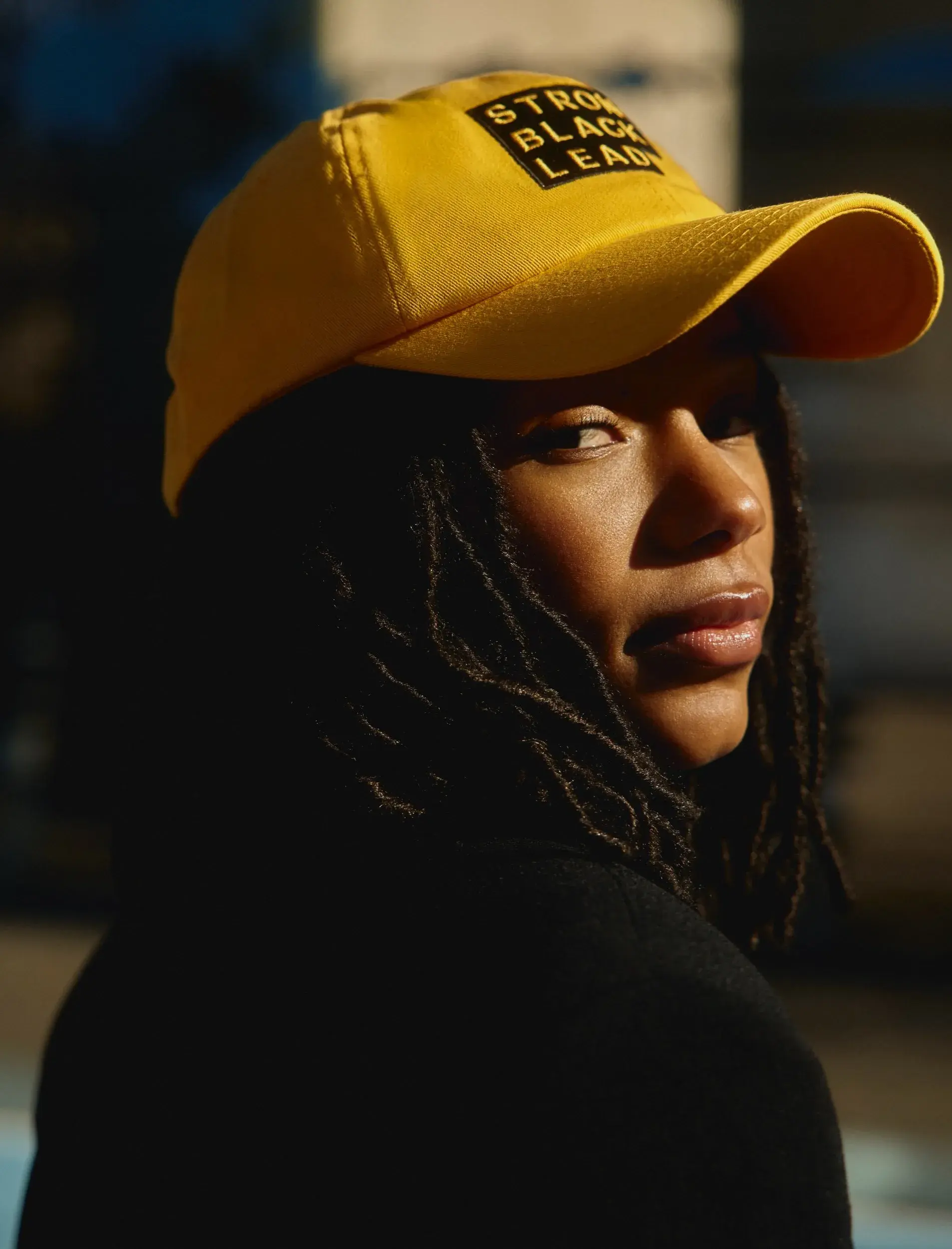 Portrait of a person wearing a yellow cap embroidered with the stepped Strong Black Lead logo in black and white.