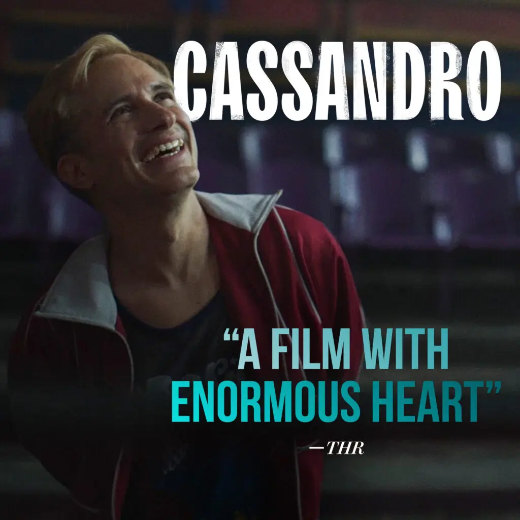A smiling person in a red jacket sits beneath the CASSANDRO title and a turquoise pull quote reading “A Film With Enormous Heart” from THR.