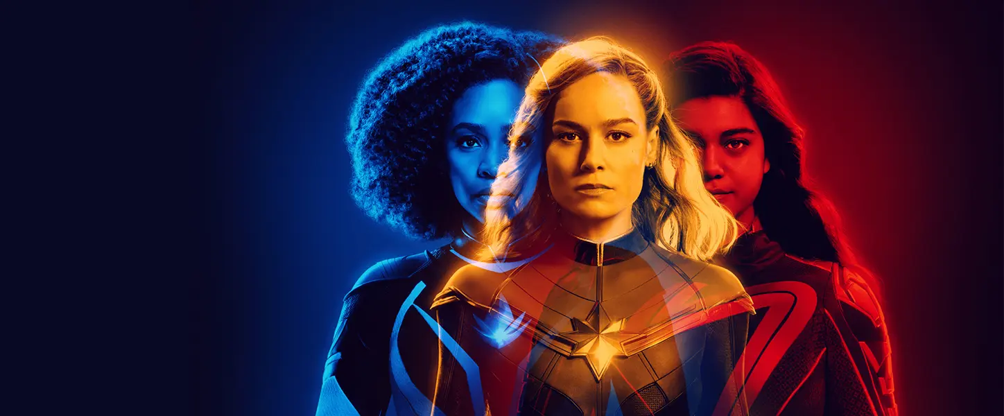 Three overlapping portraits of Monica Rambeau (blue), Carol Danvers / Captain Marvel (center, gold), and Kamala Khan / Ms. Marvel (red) with colored halos suggesting power entanglement and layered motion.