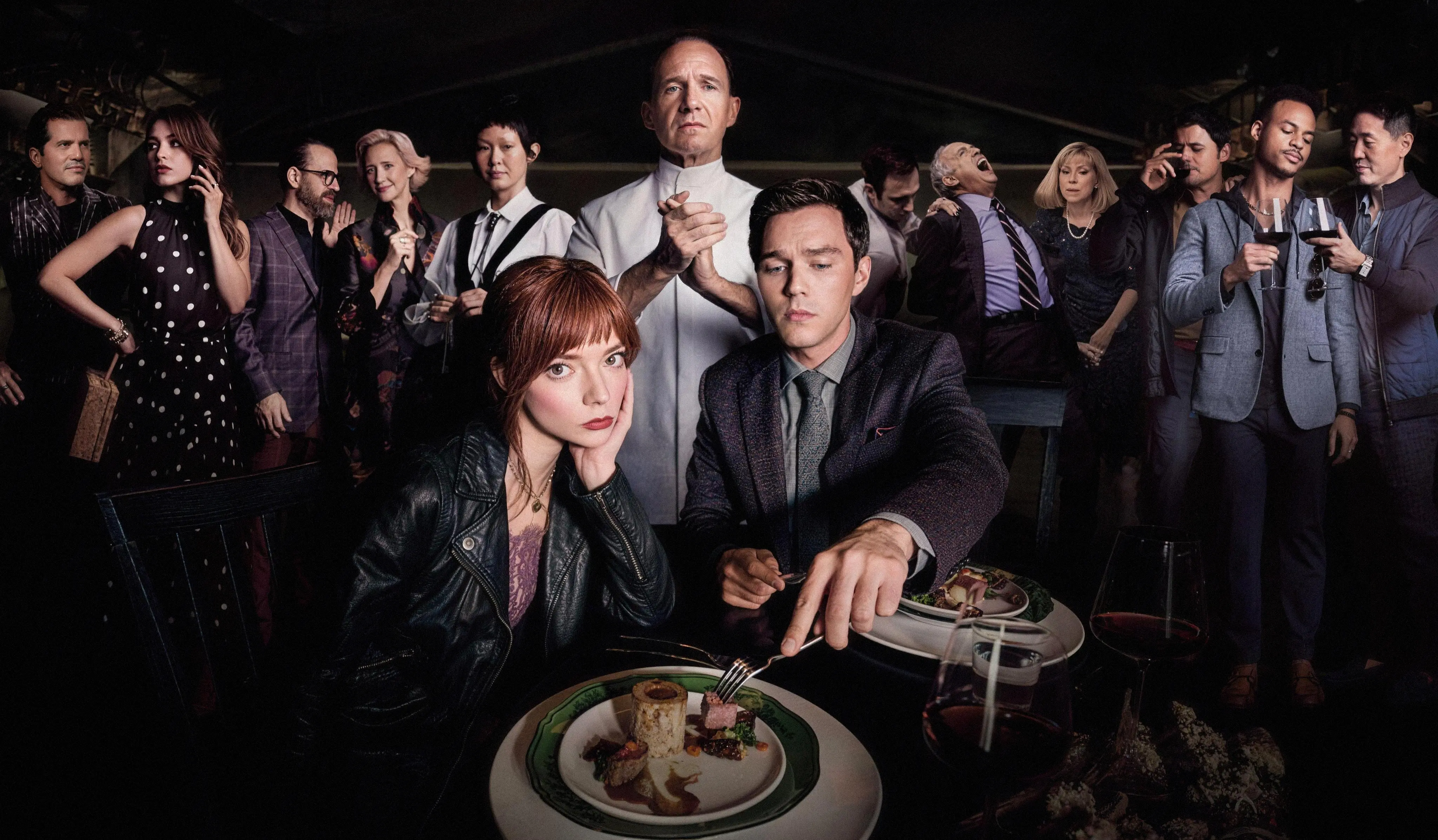 Chef Slowik stands behind Margot, Tyler, and Hawthorn’s other diners as they gather around a table set with plated food and wine.