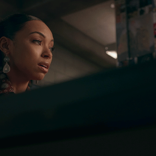 A close-up GIF of a woman wearing drop earrings as she looks to the side in a dimly lit interior.
