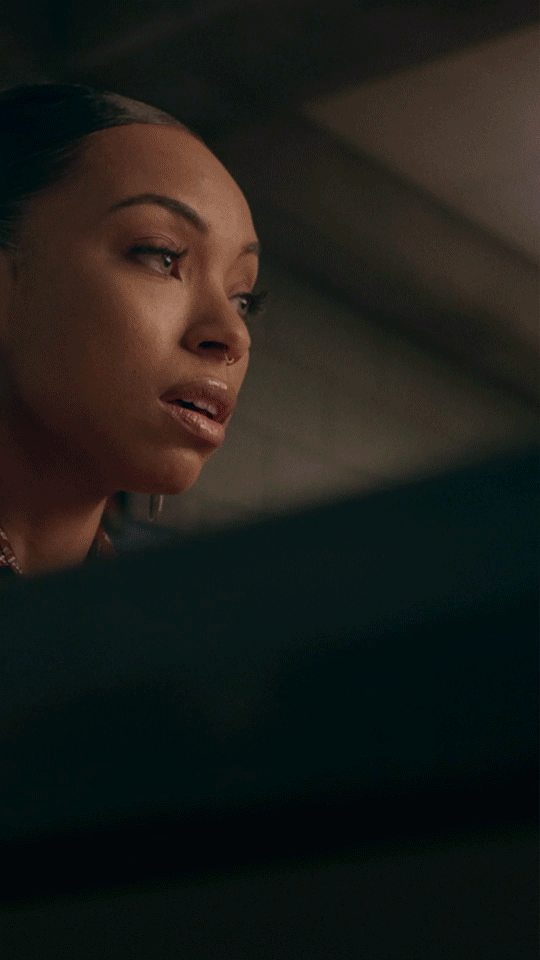 Close-up GIF of a woman looking offscreen with a quiet, contemplative expression in a dimly lit interior.